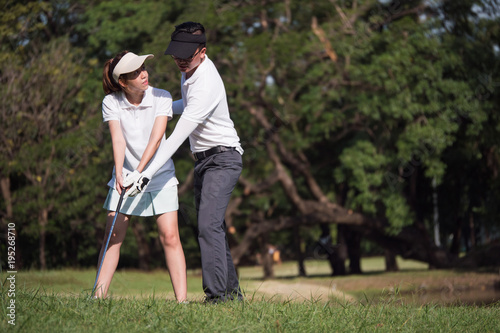 Asian young couple playing golf on golf course, the male partner is trainer to the female golfer