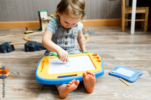 A three year old girl playing with magnetic  drawing board on the floor in her room