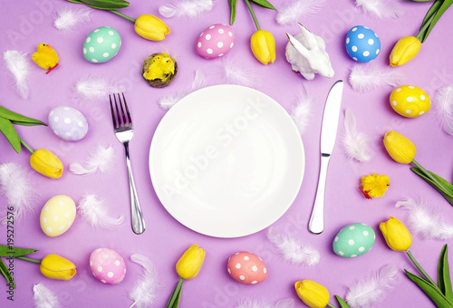 Easter table setting with cutlery, colorful eggs and tulips on violet table. Copy spase.