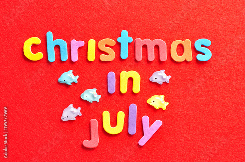 The words christmas in July in colorful letters on a red background and dolphins figurines