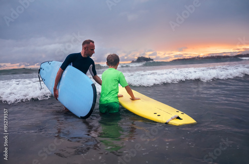 Father learning his son to surf at sunset time