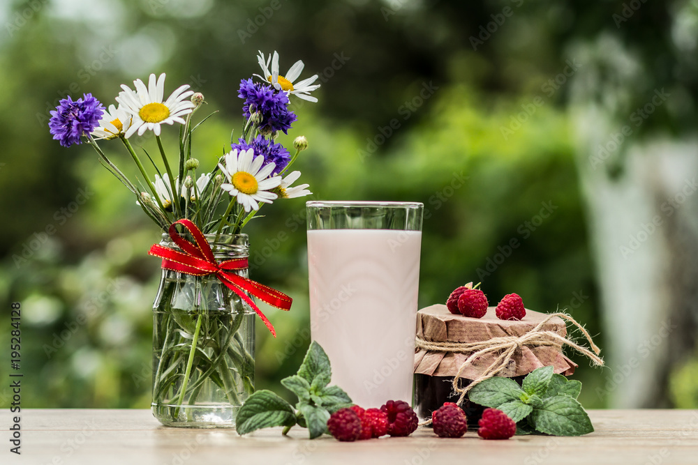 Glass of raspberry yogurt with fresh berries of raspberry. Chamomile with cornflowers in vase on the table Glass of raspberry yogurt with fresh berries of raspberry. Chamomile with cornflowers in vase on the table