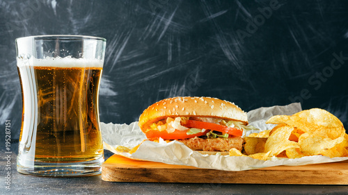 Chicken burger and glass of beer. Homemade hamburgers  pickles and chips  on wooden tray. Black metal background. Baking paper