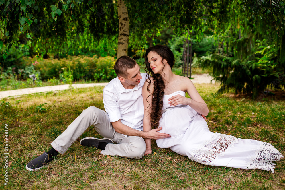 Smiling couple sitting in a beautiful garden can't wait for their baby to be born. Affectionate man and woman on romantic date in a stunning park. Expecting parents experiencing the joys of pregnancy
