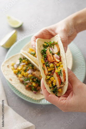 Hands holding tacos with roasted chicken meat, corn, parsley, salsa and sweet pepper.