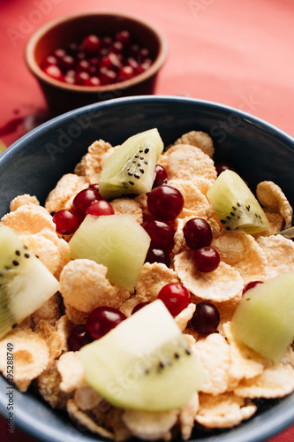 delicious crispy cornflakes with kiwi pieces and cranberries in bowl,  healthy breakfast on red background