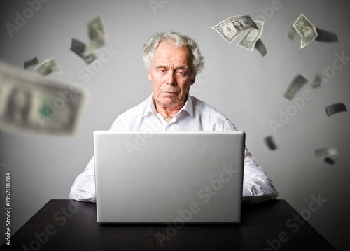 Old man using a laptop. Old man in white earns dollars on the internet.