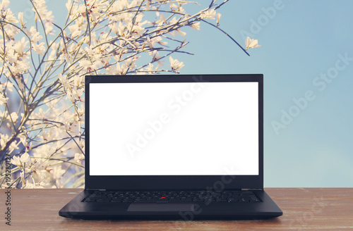 Image of outdoors with open laptop and empty white screen for copy space.