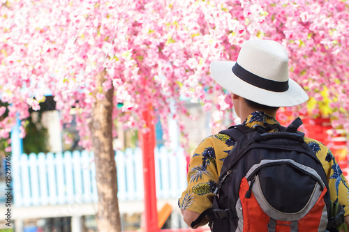 Young man wearing a vintage style shirt and brim hat. He traveled with backpack to visit and see the cherry blossoms. Soft focus and blur. Tourist concept. Photo in cool tone.