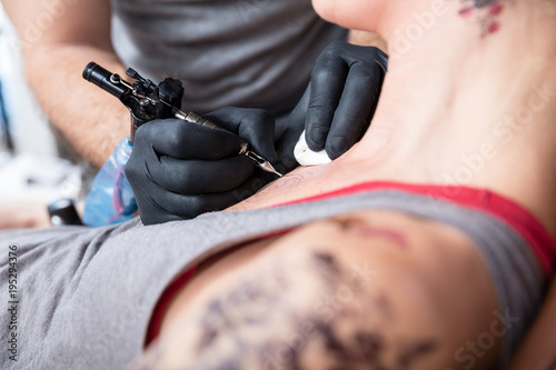 Close-up of the hands of a tattoo artist wearing black gloves while tattooing two roses on the chest of a trendy woman