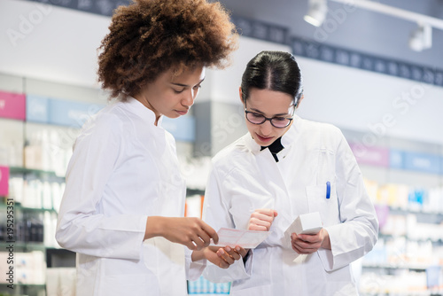 Canvastavla Two female pharmacists reading the information from the pack of a new product wh