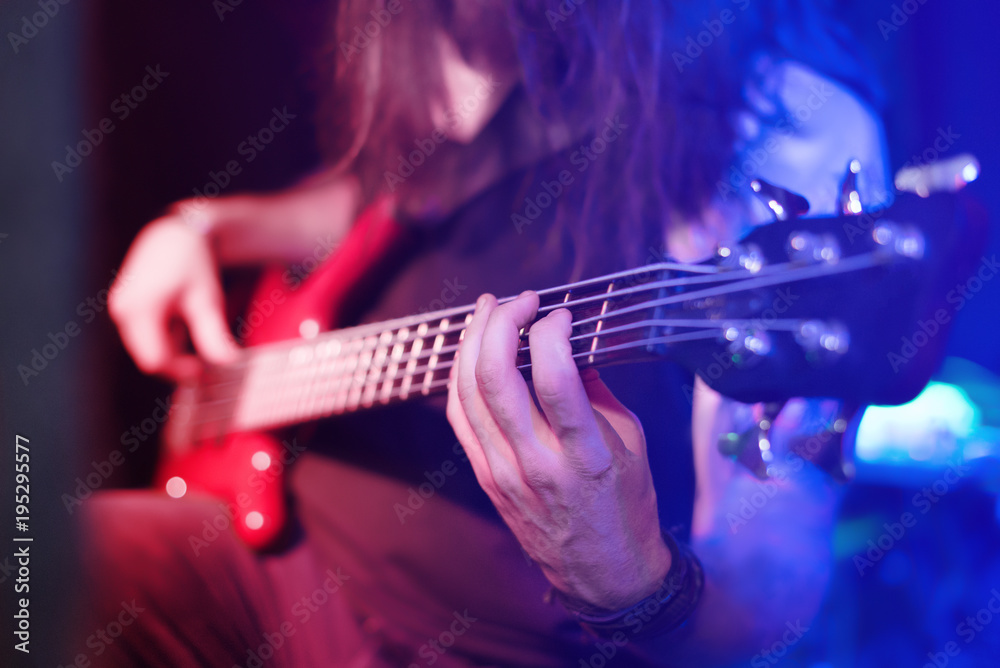 Obraz premium The bass guitar player is on stage in the bright red and blue lights of the spotlights. Selective focus.