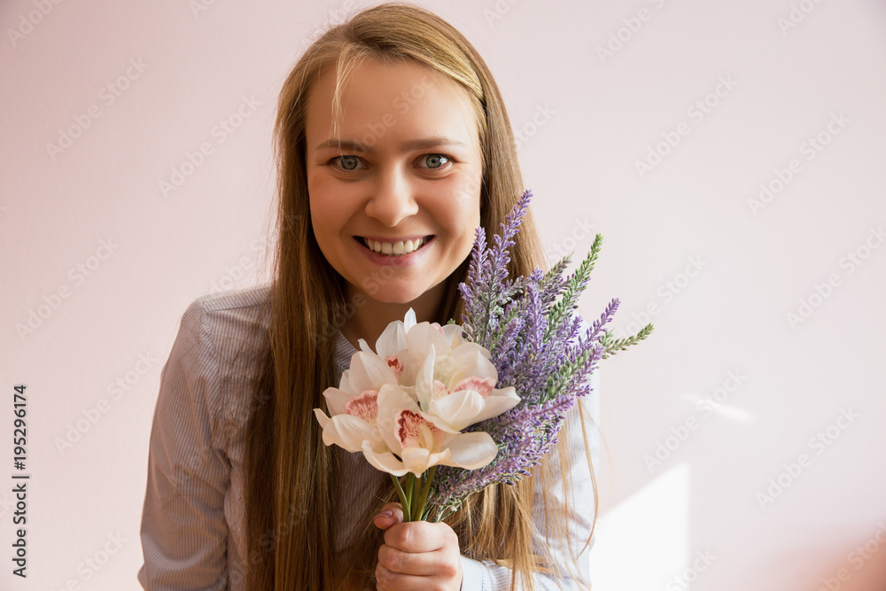 A young beautiful girl with blond long loose hair, keeps spring flowers in the hands of a sunny day. She smiling. Copy space. A young beautiful girl with blond long loose hair, keeps spring flowers in the hands of a sunny day. She smiling. Copy space.