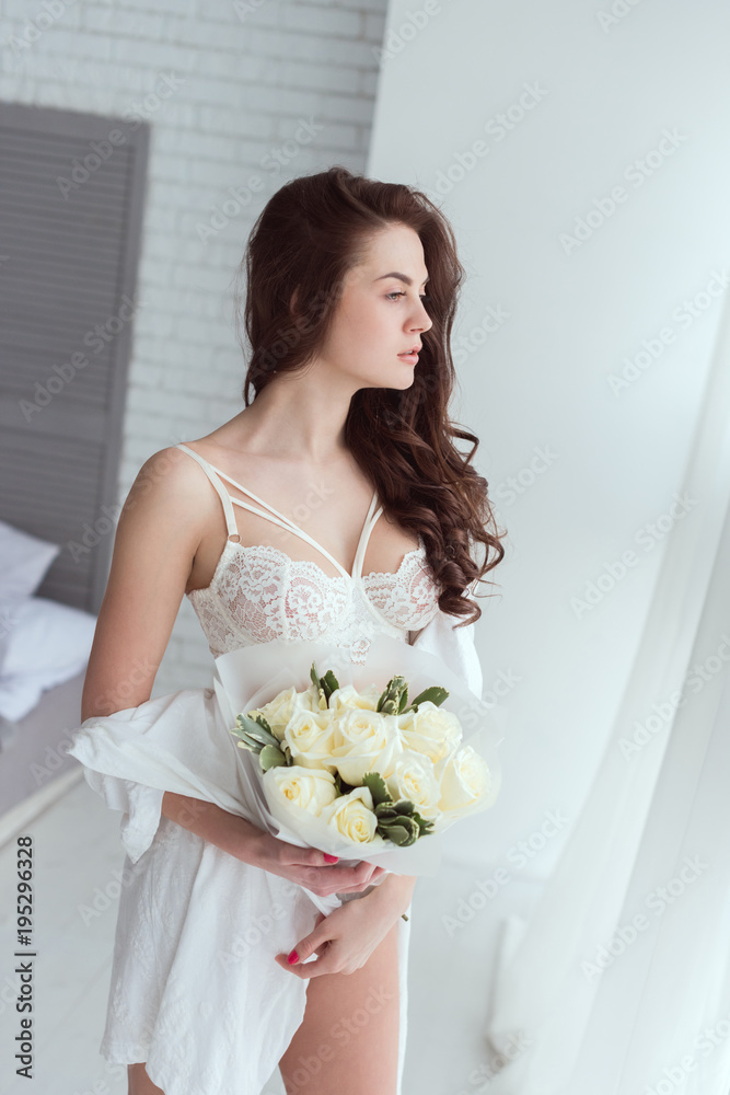 young pensive woman in underwear with bouquet of roses looking out window young pensive woman in underwear with bouquet of roses looking out window