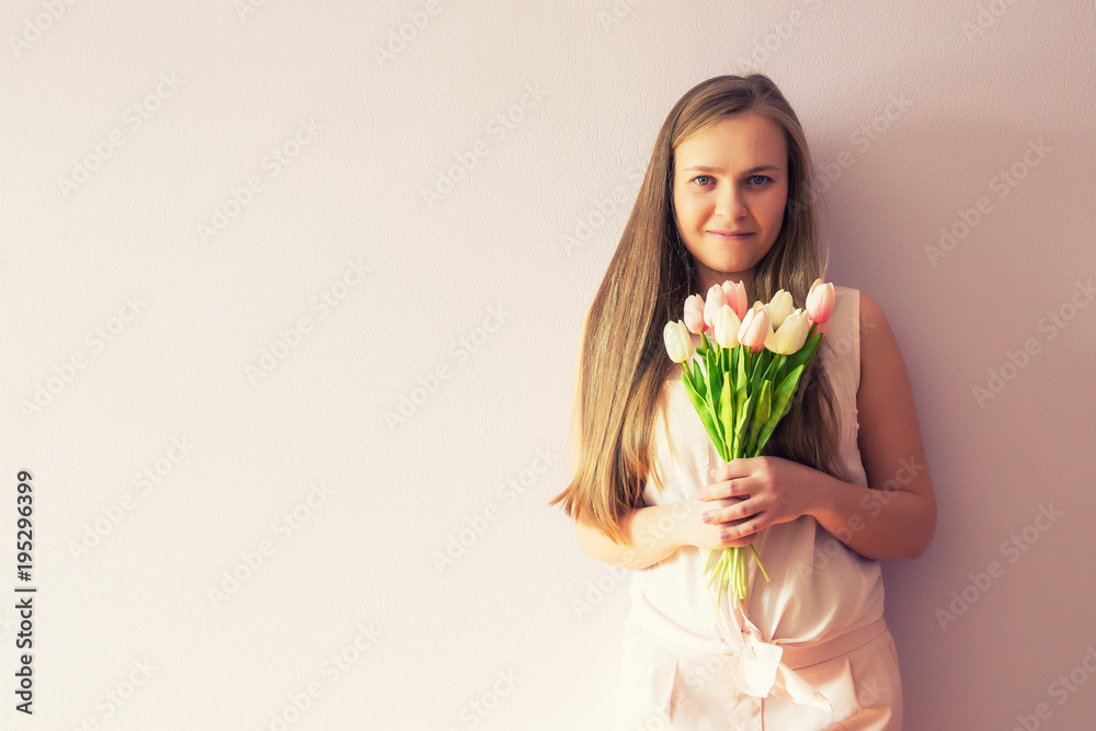 A young beautiful girl with blond dissolved long hair, a felt hat on her head, keeps spring flowers in her hands on a sunny day. Women's Day. A young beautiful girl with blond dissolved long hair, a felt hat on her head, keeps spring flowers in her hands on a sunny day. Women's Day.