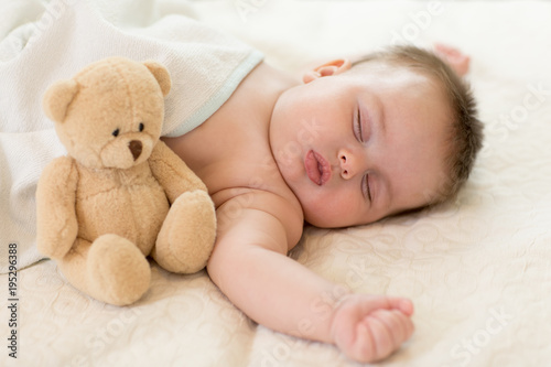 Sleeping baby in bed with teddy bear.