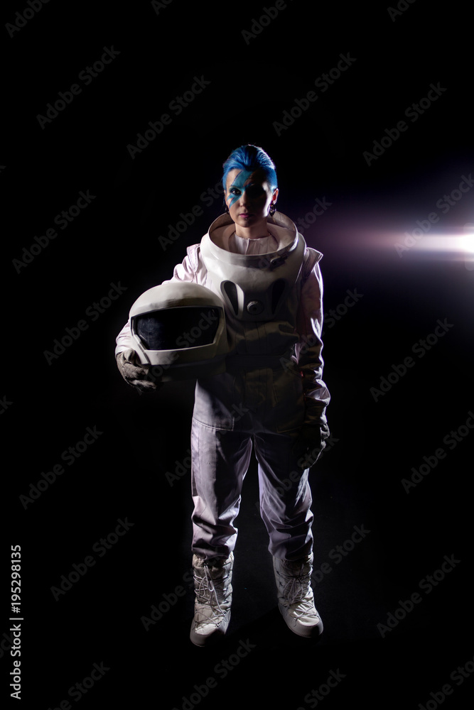 Astronaut on a black background, a young woman with face art in the space suit. Helmet in hands Astronaut on a black background, a young woman with face art in the space suit. Helmet in hands