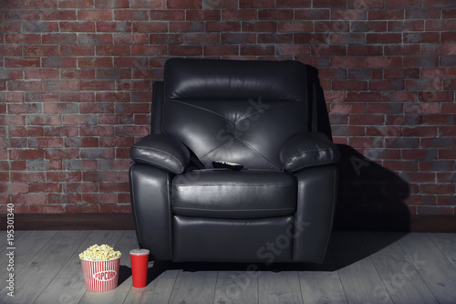 Comfortable armchair with remote control, popcorn and drink in home cinema. Watching movie © Africa Studio
