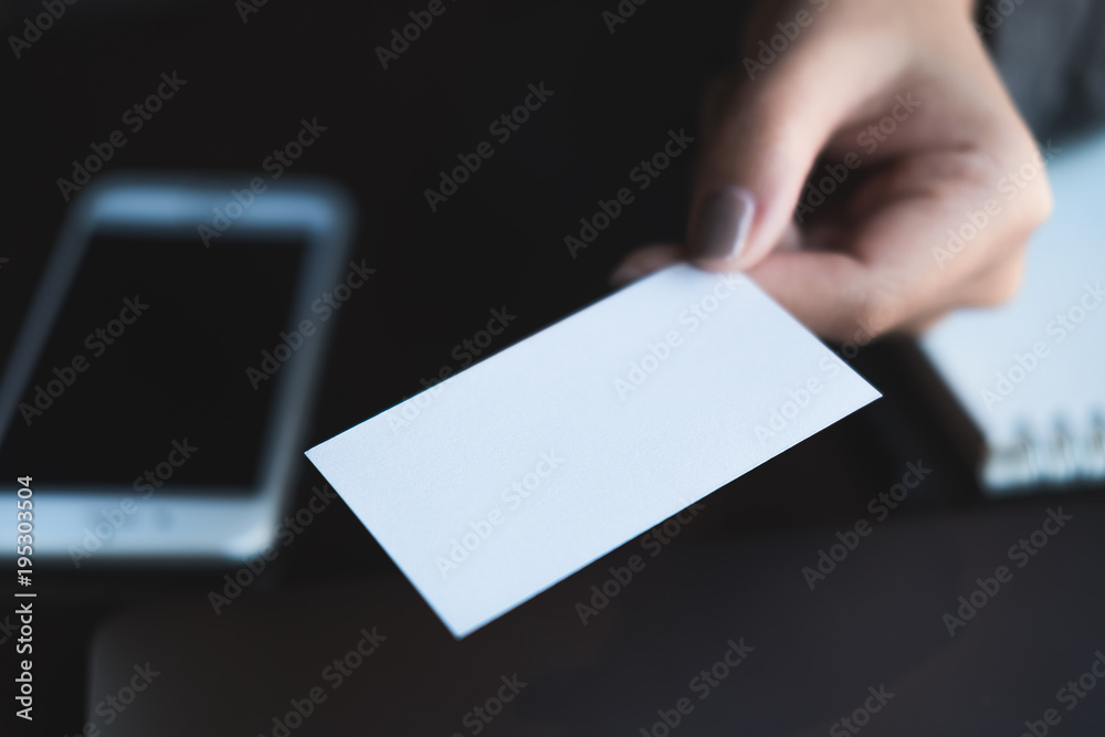 Obraz premium Business woman holding and giving business card to someone with mobile phone and notebook on table in office