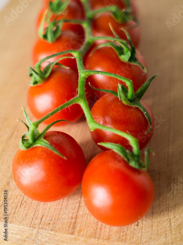 Little branch of cherry tomatoes over wooden background.
