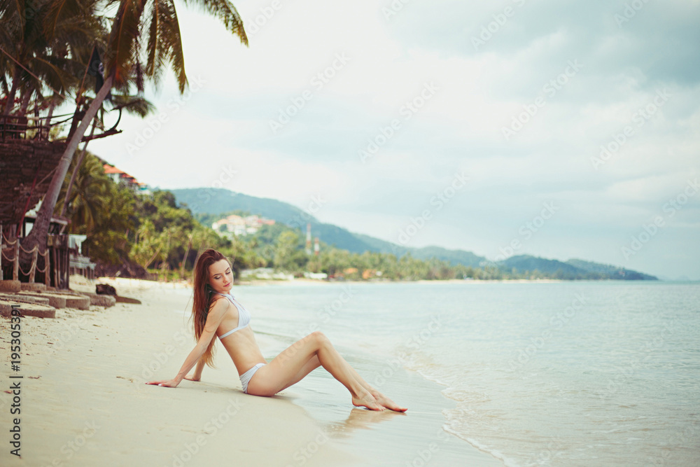 Side view of young woman in bikini resting on beach near ocean