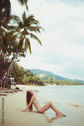 side view of young woman in bikini resting on beach near ocean