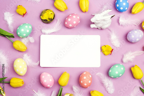 Empty paper card with colored eggs, feathers and tulip on violet background. Space for text.
