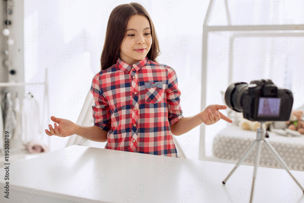Interesting story. Happy pre-teen girl in a checked shirt filming a video blog and telling her viewers about her day while gesticulating Interesting story. Happy pre-teen girl in a checked shirt filming a video blog and telling her viewers about her day while gesticulating