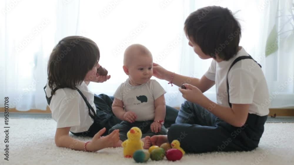 Three cute boys, siblings, brothers, playing with Easter eggs, eating chocolate bunnies at home, sunny living room Three cute boys, siblings, brothers, playing with Easter eggs, eating chocolate bunnies at home, sunny living room