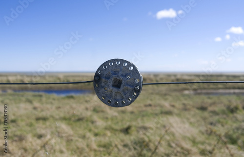 Laesoe / Denmark: Close-up of an aluminium fence tensioner in front of the salt marsh at Bovet Bugt photo