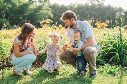 Young happy family having fun in flowers outdoors. Couple in love holding their cute children. Mother father daughter son.