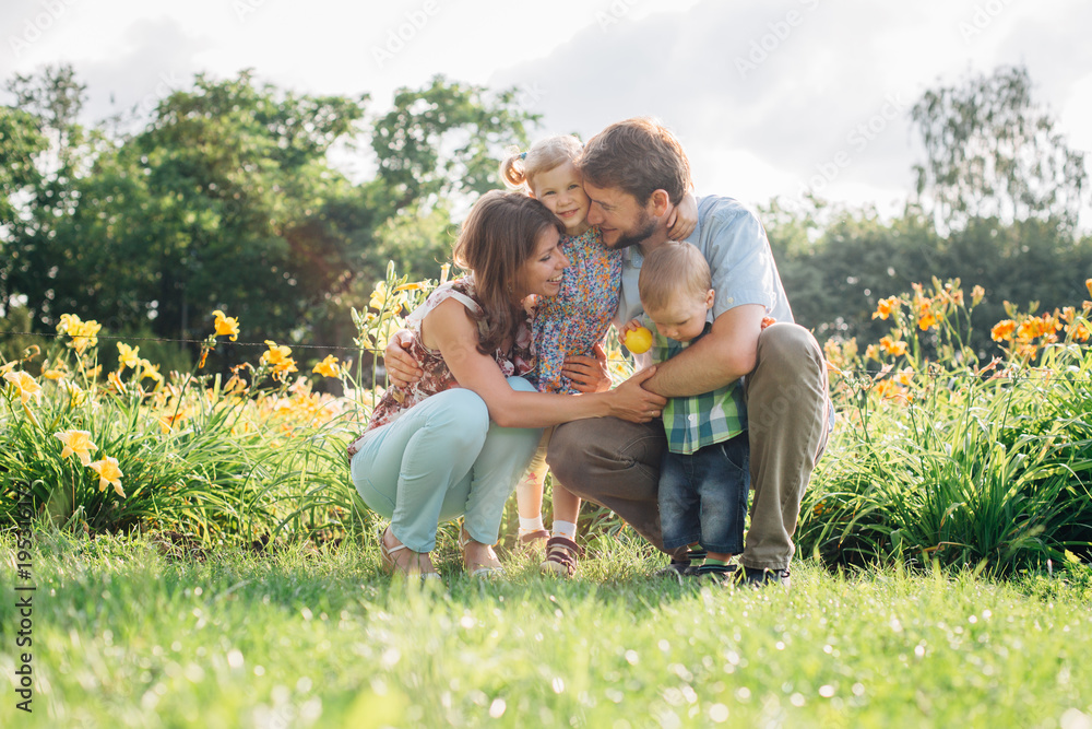 Young happy family having fun in flowers outdoors. Couple in love holding their cute children. Mother father daughter son.