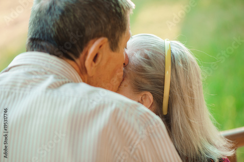 Embrace and kiss of old couple in a park on a sunny day