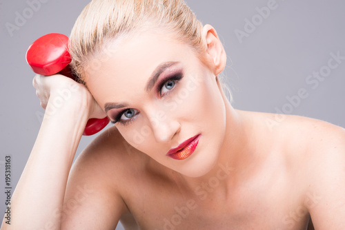 Beautiful young model wearing make-up holding dumbbell.