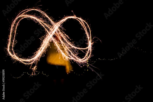 A young woman playing with sparklers at night creating an infinity symbol.