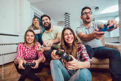 Group of friends play video games together at home, having fun. © Mediteraneo