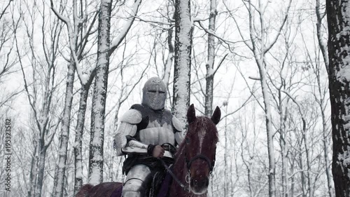 Portrait of brave medieval knight wearing steel protection and helmet, being horseback on battlefield in forest slow motion. Reconstruction of historical battle