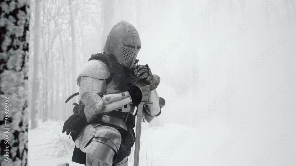 Portrait of medieval warrior armed with steel weapon standing on one knee on winter nature, in slow motion. Reconstruction of ancient times