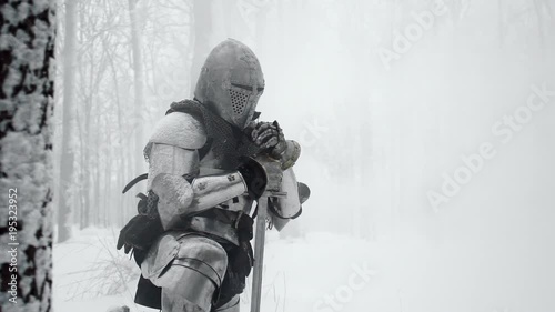 Portrait of medieval warrior armed with steel weapon standing on one knee on winter nature, in slow motion. Reconstruction of ancient times