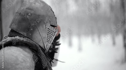 Portrait closeup of male soldier in profile wearing like medieval warrior putting on visor of steel helmet, while walking in winter wood slow motion. Fantasy and reenactment