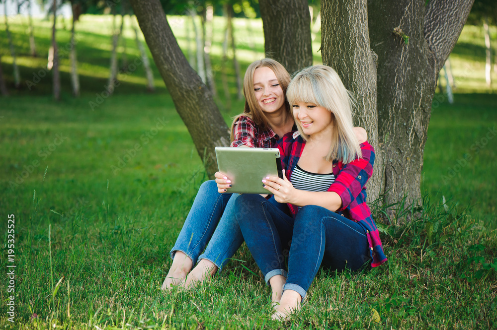 Smiling women using tablet ps on a green meadow Smiling women using tablet ps on a green meadow
