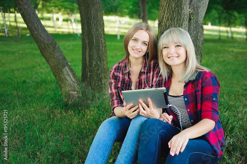 Two happy friends searching media content online in a laptop sitting on the grass in a park