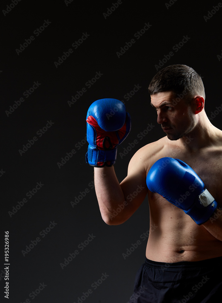 Low key studio portrait of handsome muscular fighter practicing boxing on dark blurred background