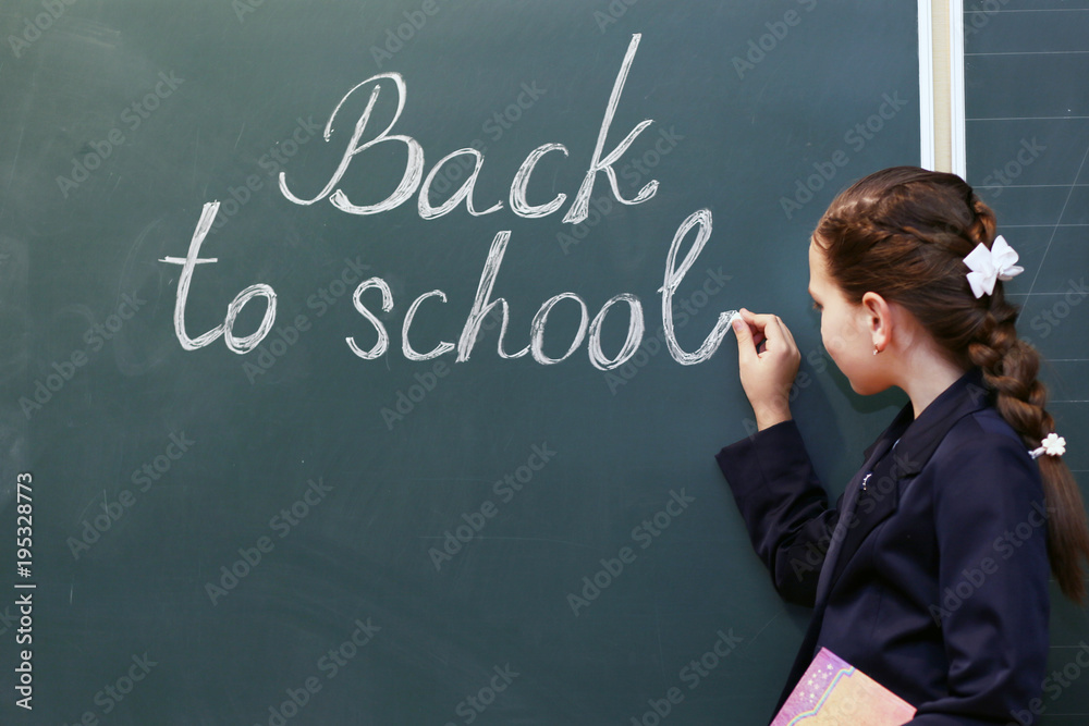 Child schoolgirl writes on blackboard back to school