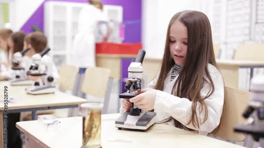 Little girl is looking through a microscope at a lesson in school Little girl is looking through a microscope at a lesson in school