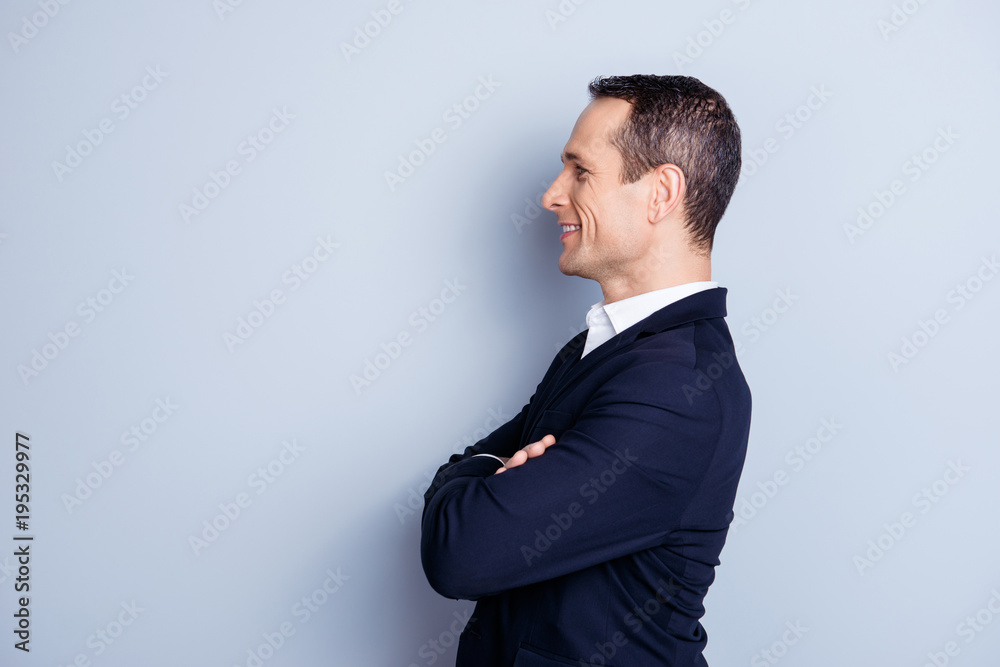 Profile, side view portrait of cheerful, caucasian, smiling, attractive politician in formal wear, having his arms crossed, standing over gray background Profile, side view portrait of cheerful, caucasian, smiling, attractive politician in formal wear, having his arms crossed, standing over gray background