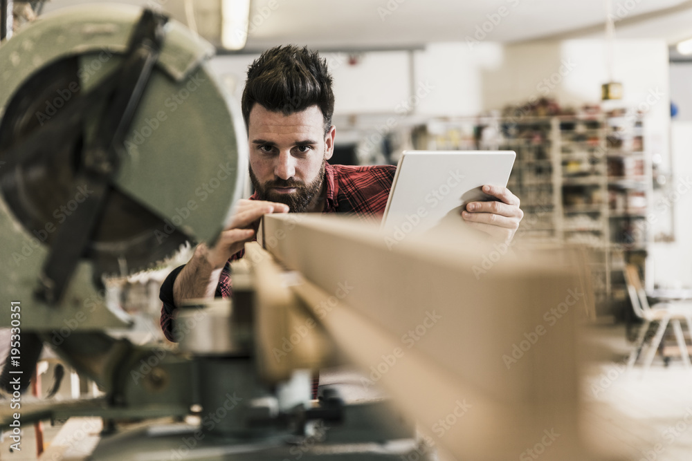 Man in workshop with piece of wood and tablet