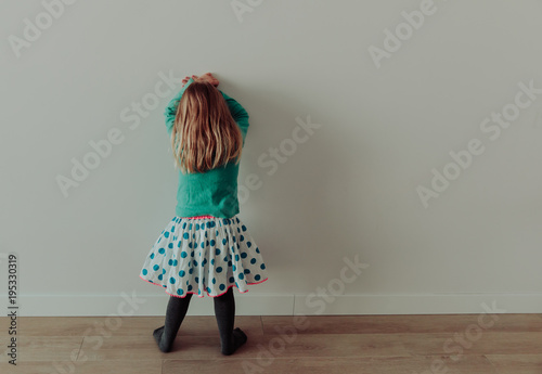 Little girl standing up against a wall