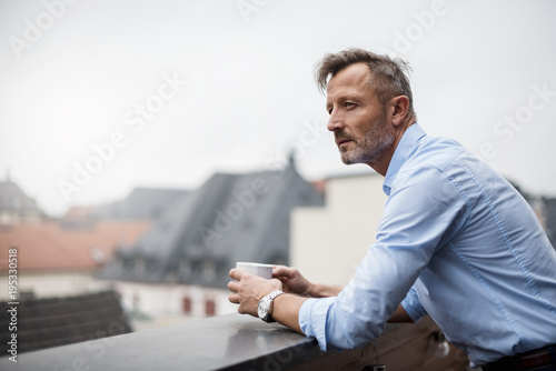 Portrait of mature businessman with cup of coffee on roof terrace photo