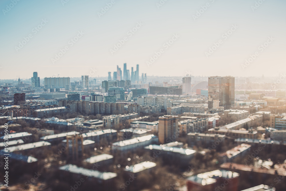 True tilt-shift view of autumn or spring cityscape with skyscrapers and residential houses, with focus on the middle zone of the image; background and foreground are blurred and have strong bokeh